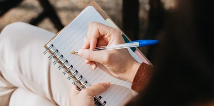 A woman writing in a notebook with a pen.