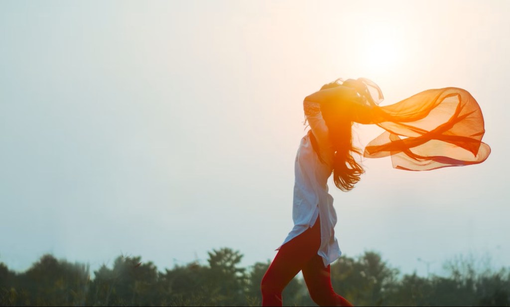 A woman in the sun dancing with a flowing scarf.