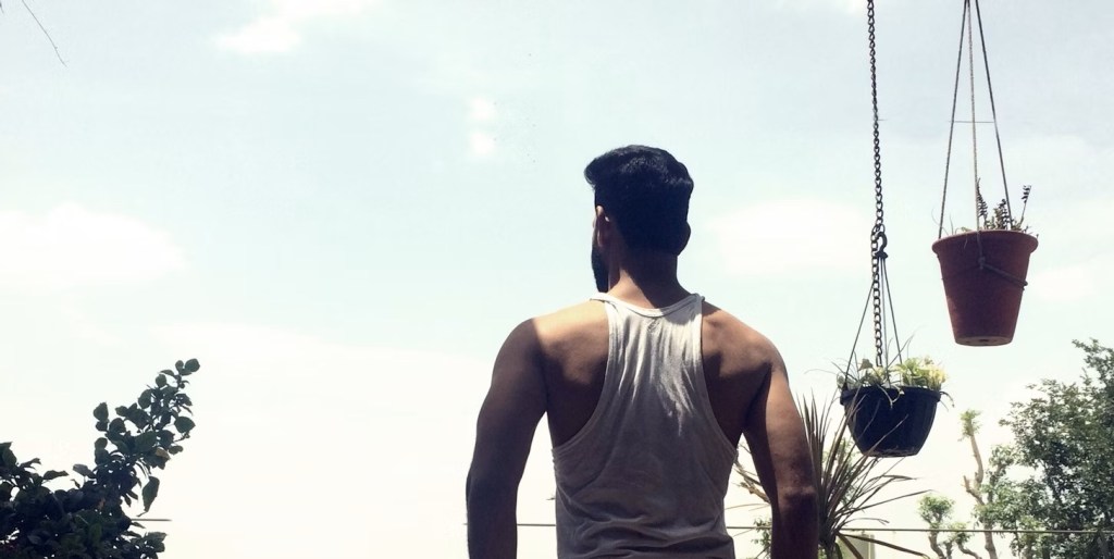 Healthy young man standing outside shown from behind.