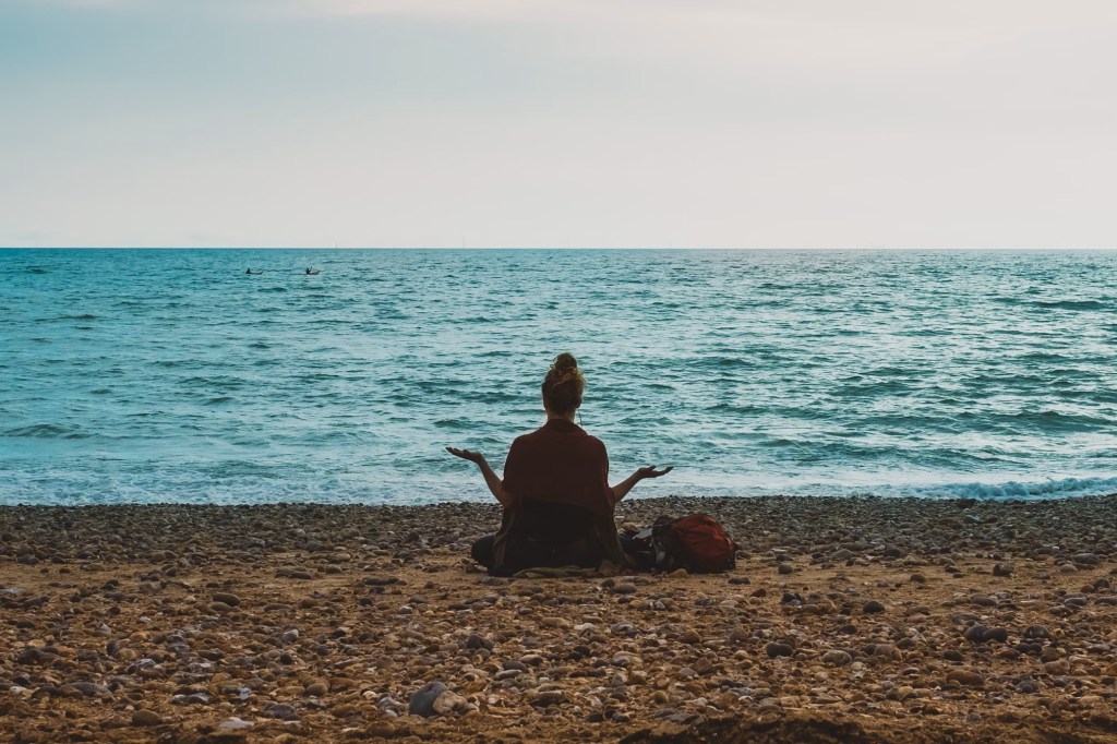 Woman on a beach at a distance meditating.