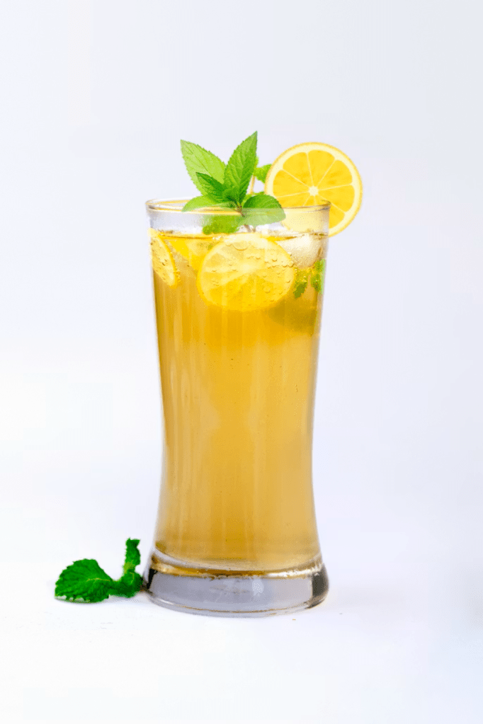 Tall yellow iced drink with mint springs and lemon slices.